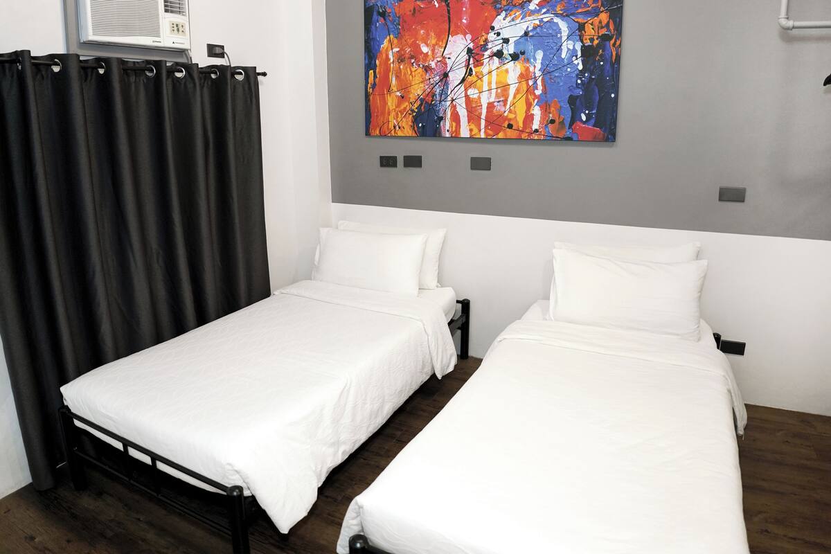 A room with two single beds, a large abstract painting on the wall, and a black curtain.