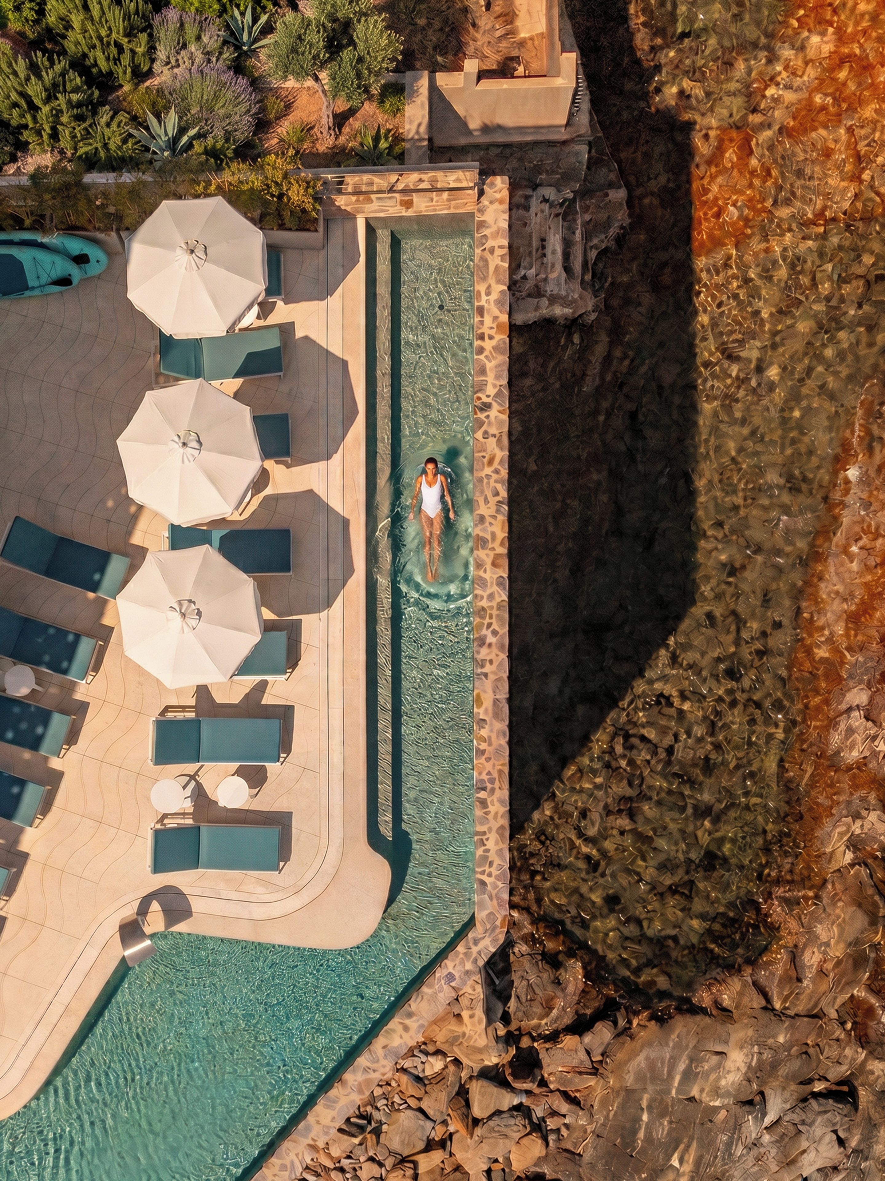 Una piscina con sillas de descanso y sombrillas, rodeada por un acantilado rocoso.