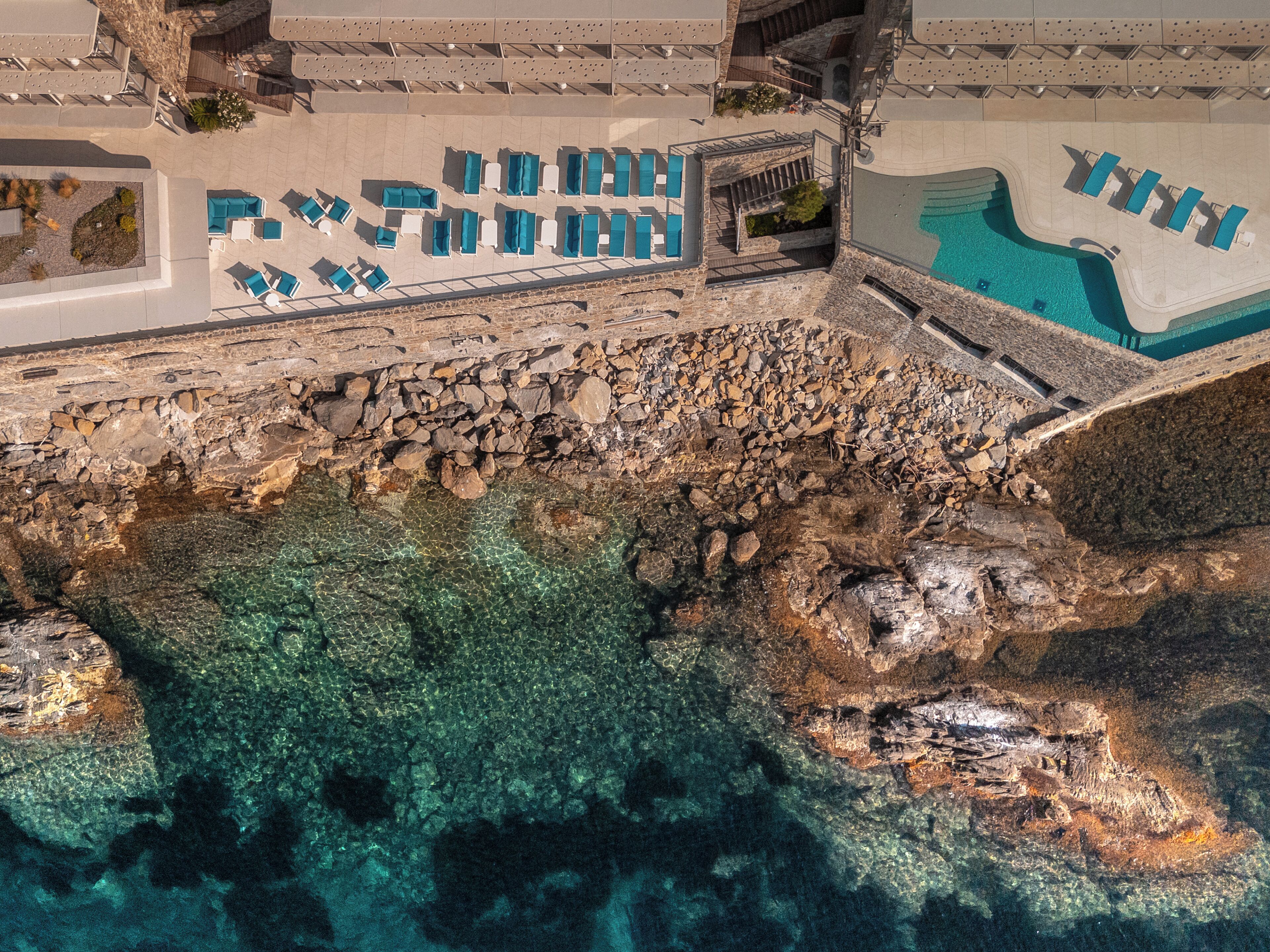 Un resort con piscina, mobiliario exterior y un litoral rocoso.