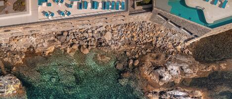 Un resort con piscina, mobiliario exterior y un litoral rocoso.