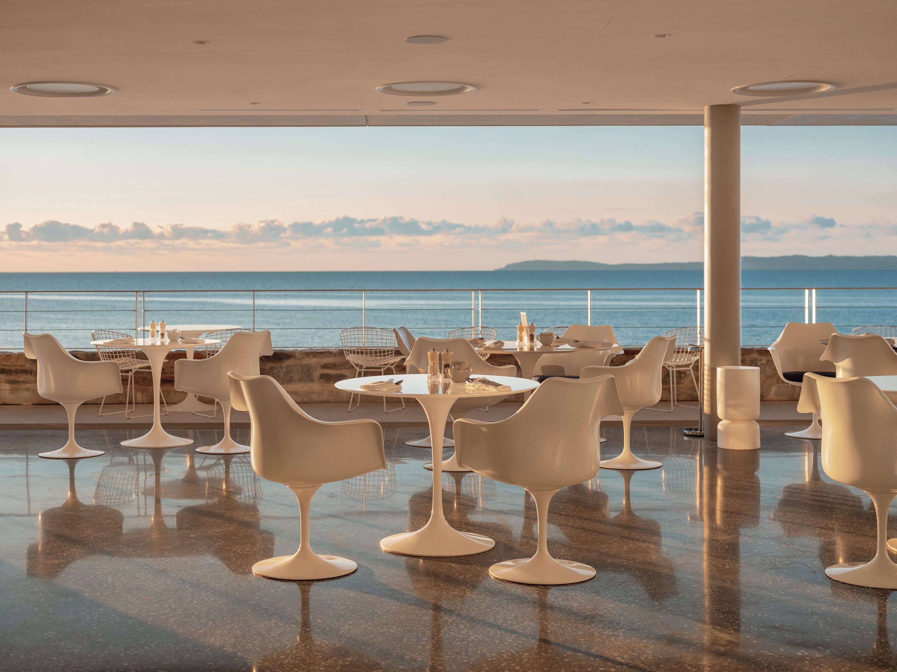 A modern outdoor dining area with white chairs and tables, overlooking a body of water.