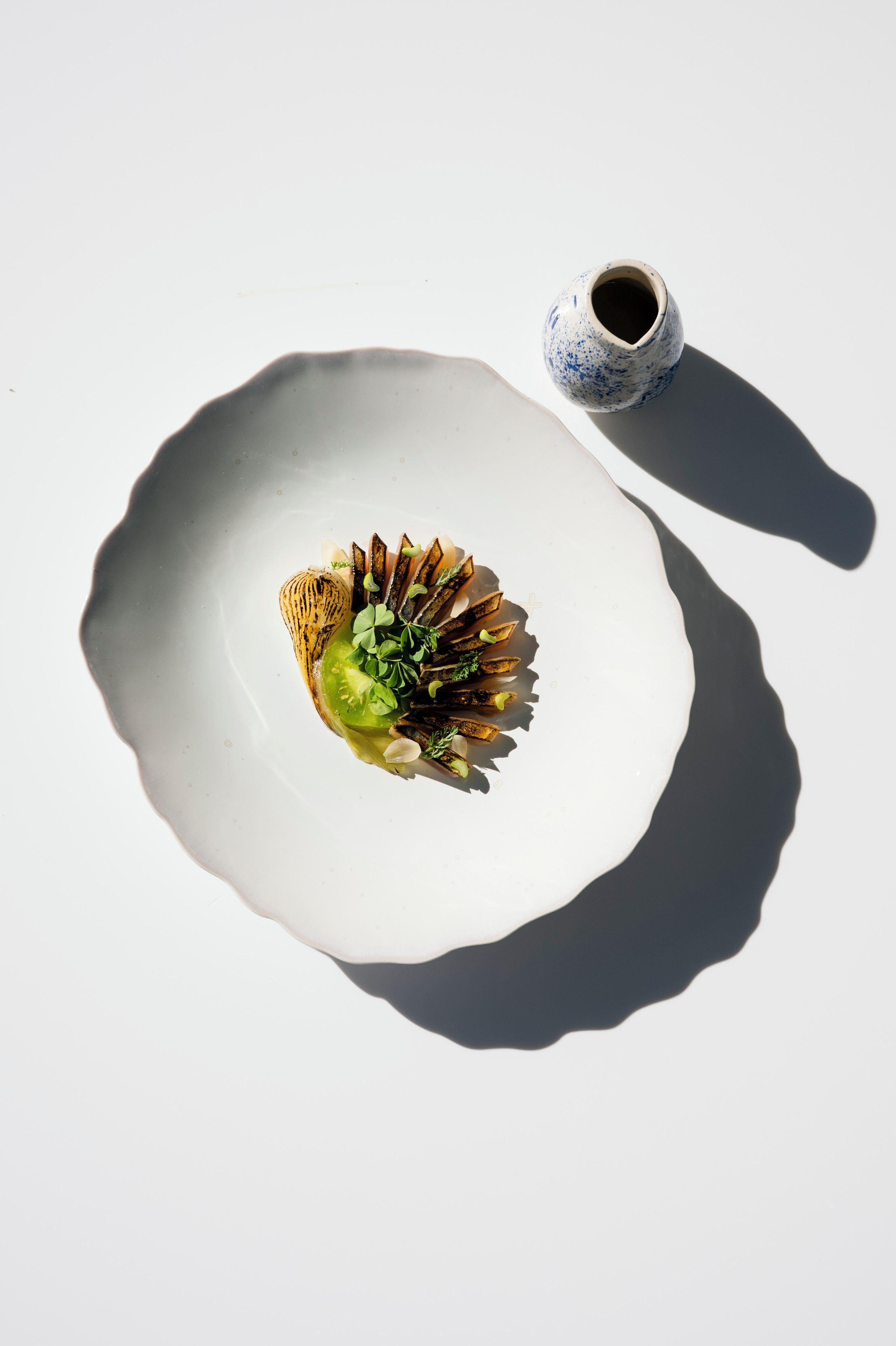 A white plate with a dish of food and a small blue and white ceramic cup.