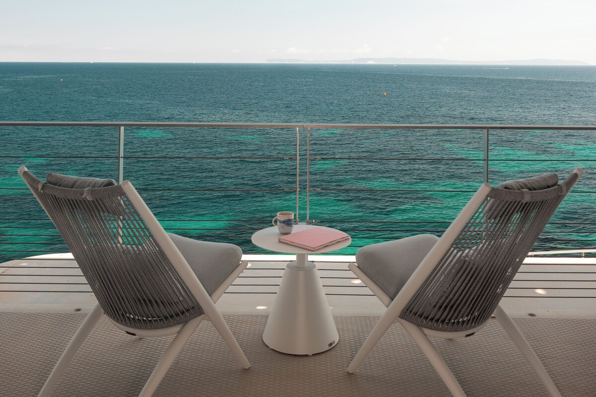 A balcony with two wicker chairs, a small table, and a view of the ocean.