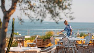 Un restaurant en bord de mer, avec une terrasse, une vue sur l’océan et un serveur qui s’occupe des tables.