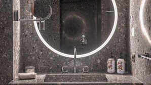 Un baño moderno con encimera de granito, un espejo redondo, un lavabo con grifo y dos dispensadores de jabón.