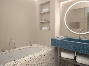 Um banheiro moderno com banheira livre, pia com bancada azul com aspecto marmorizado e espelho redondo com moldura iluminada.