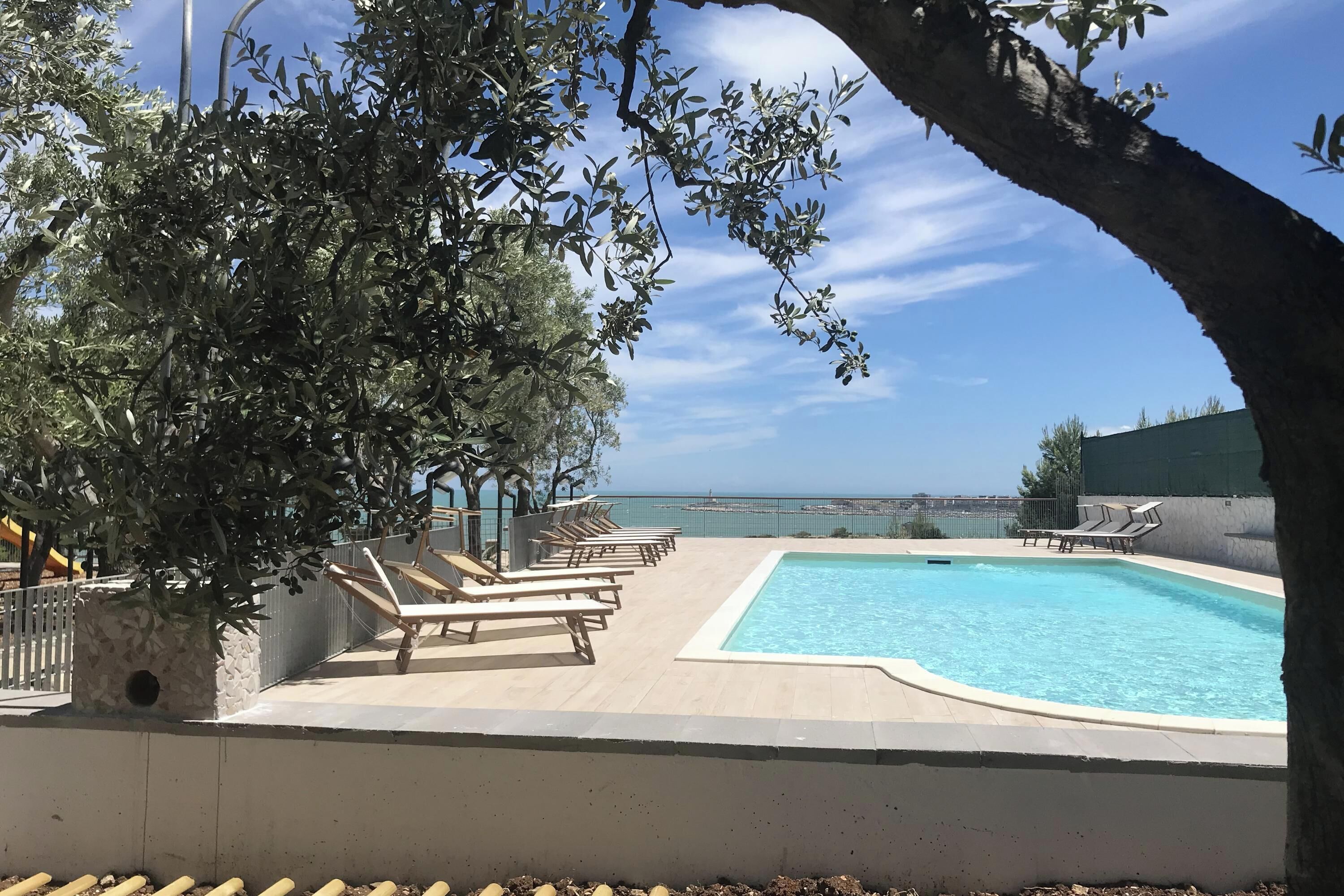 A pool area with lounge chairs, a stone planter, and a view of the sea.