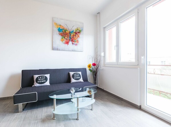 A modern living room with a grey sofa, two cushions with text, a glass coffee table, and a colorful butterfly painting on the wall. - Spacious Zadar Apartments Near Beach (Zadar)