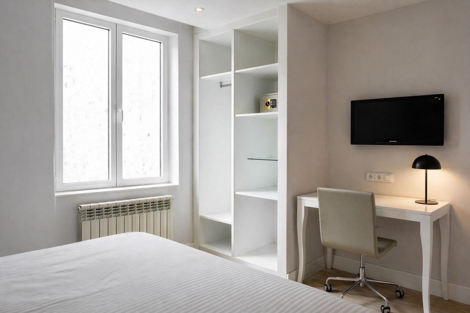 A bedroom with a bed, a desk with a chair, a TV, and built-in shelving.