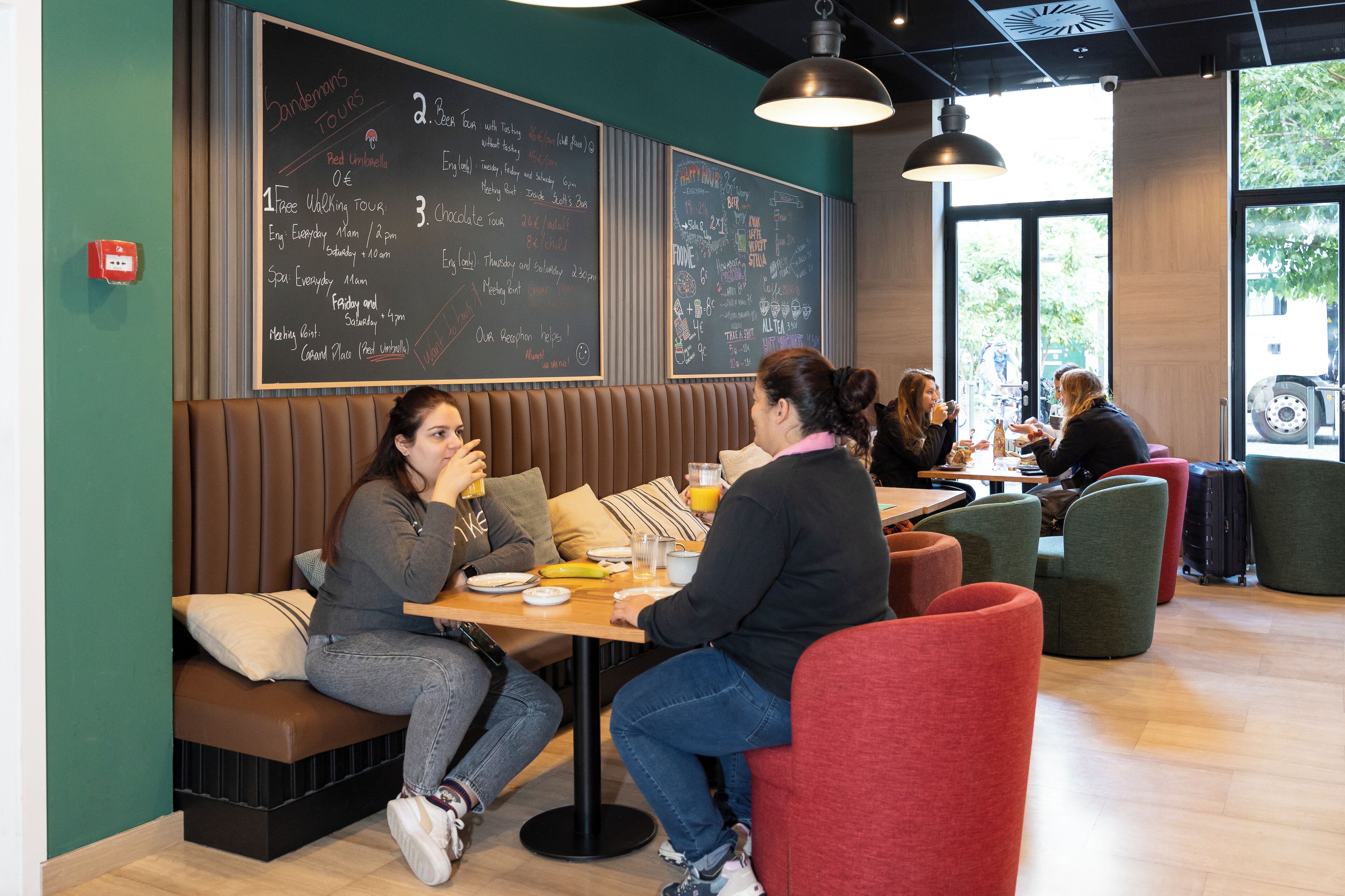 Un restaurante con cabinas y mesas, un menú en una pizarra y ventanas grandes.