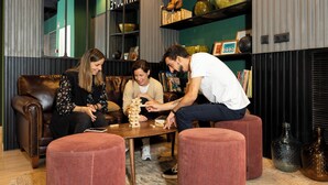 Un grupo de personas jugando un juego de mesa en una habitación con un sofá, reposapiés y estantes decorados con objetos.