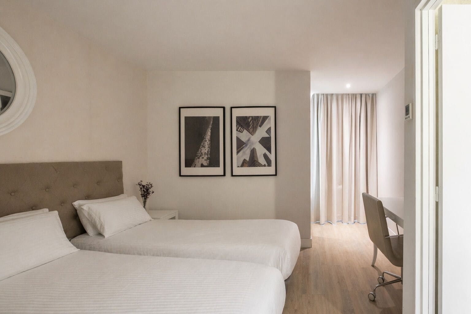 A hotel room with two beds, a desk, and a chair. There are two framed pictures on the wall.