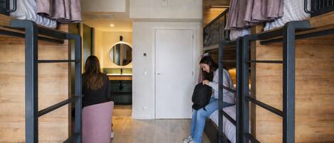 Un dormitorio con literas, un espejo redondo, una puerta y una pequeña silla rosa.