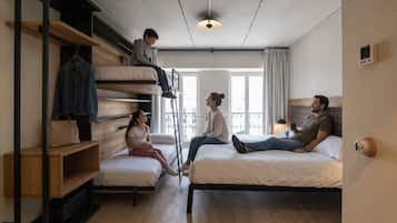 Een slaapzaal met stapelbedden, een trapje, een klein houten plankje en een raam met gordijnen.