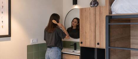 Un baño con tocador de madera, espejo, lavabo y literas.