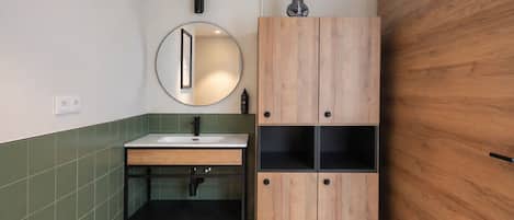Un baño con tocador de madera, espejo redondo y lavamanos.