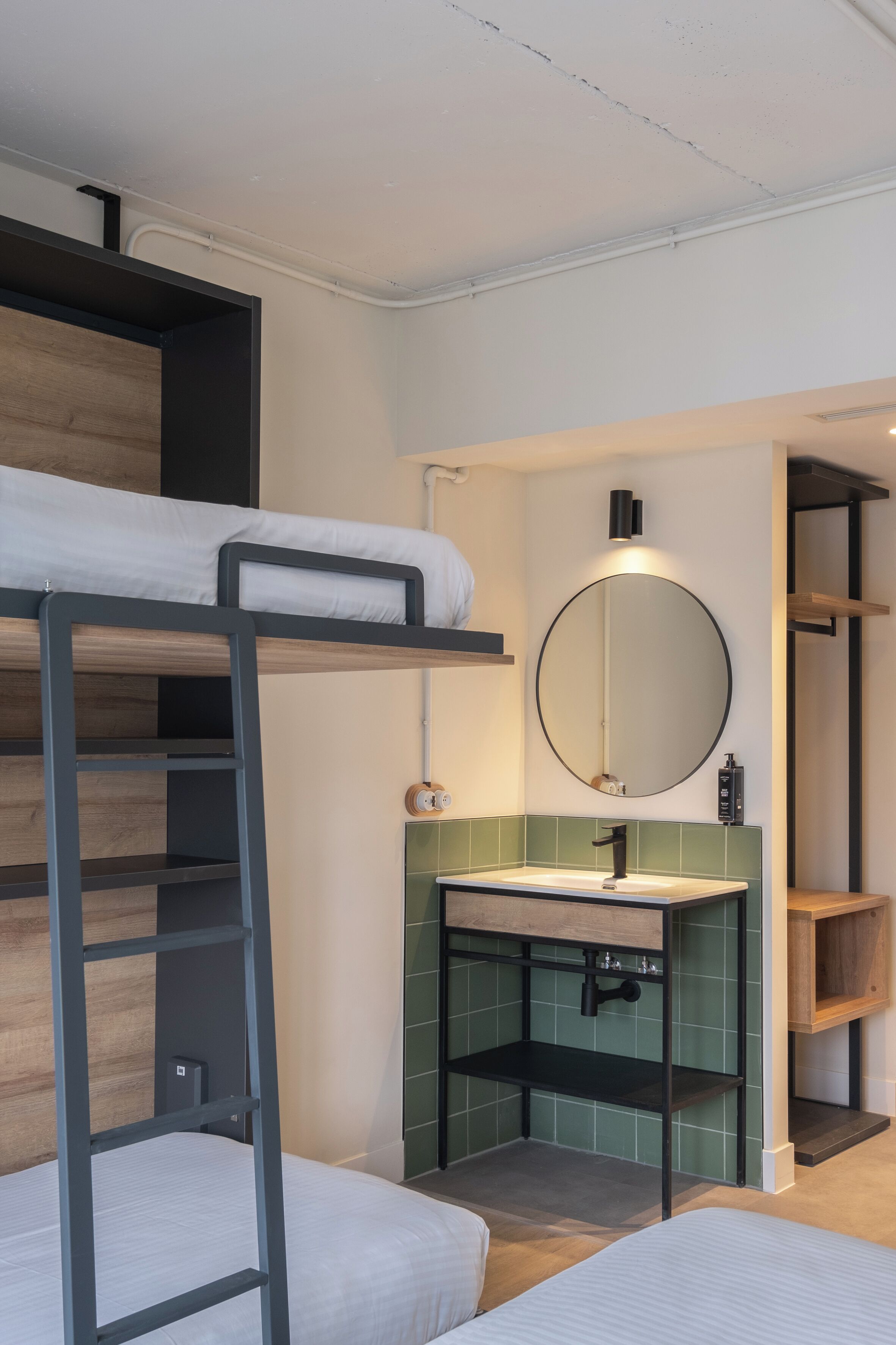Habitación con literas, cabecera de madera, mesita de noche pequeña y zona de lavamanos con cerámica verde y espejo superior.