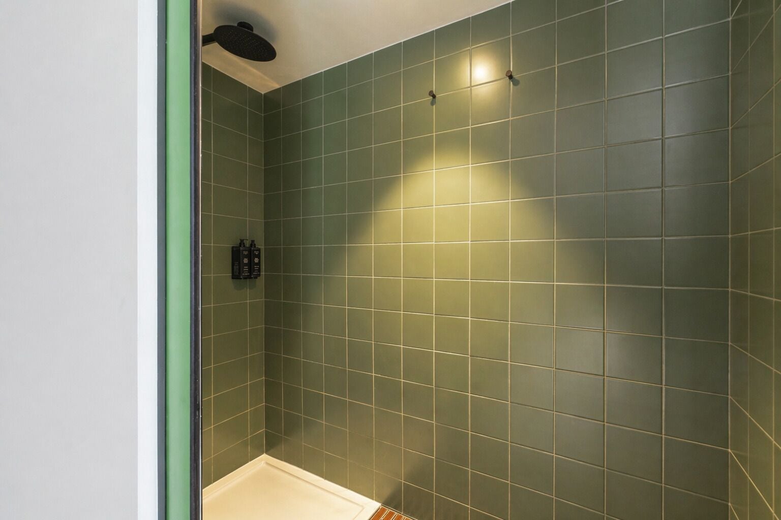 A bathroom with green tiles, a showerhead, and a towel rack.