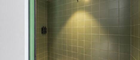 A bathroom with green tiles, a showerhead, and a towel rack.