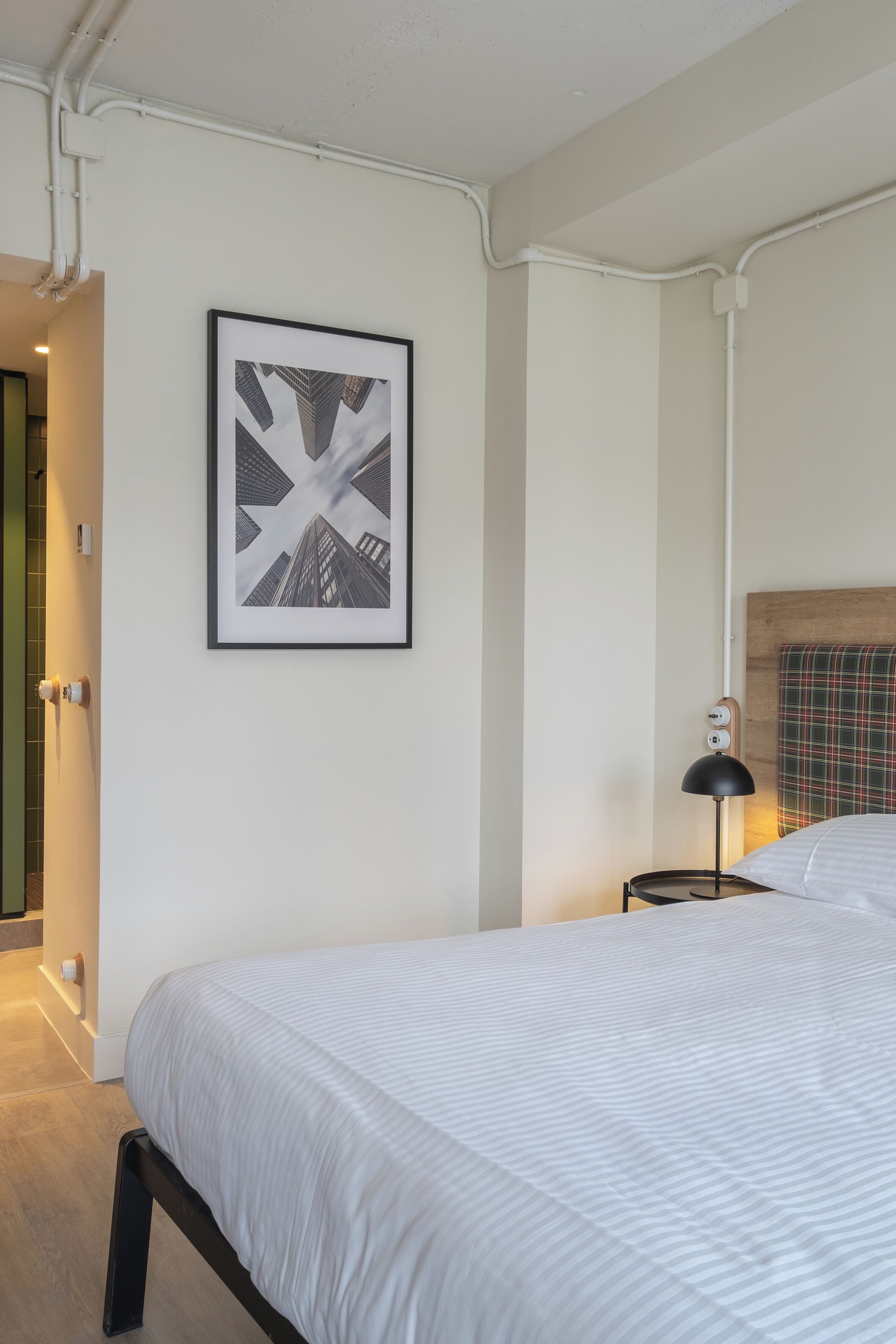 Een hotelkamer met een groot bed, een ingelijst schilderij aan de muur, een bedlampje en een geruit hoofdeinde.