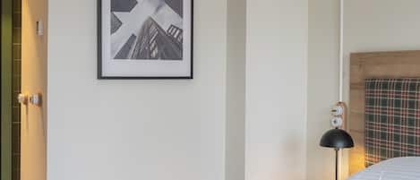 Habitación de hotel con una cama grande, un cuadro enmarcado en la pared, una lámpara de noche y un cabecero de cuadros.