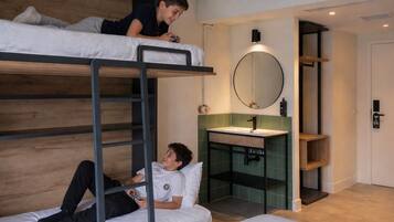 Habitación con literas y un baño pequeño que incluye un lavamanos y un espejo.