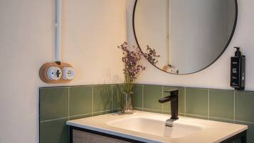 Un baño con lavamanos blanco, azulejos verdes, un espejo y un florero con flores.