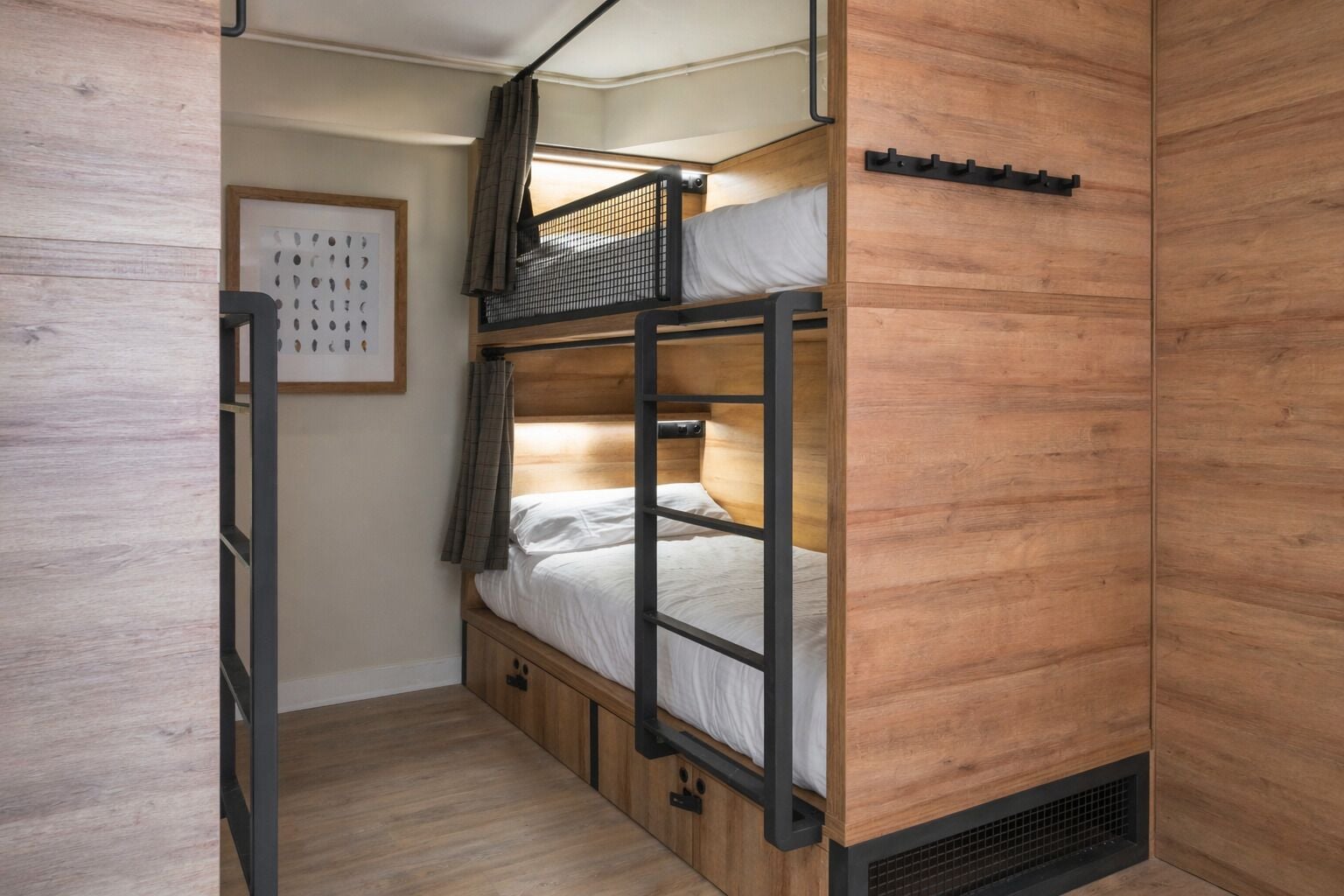 A bunk bed room with a wooden floor, a ladder, and a framed picture on the wall.