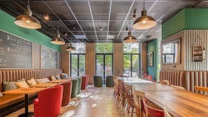 Un restaurante con una larga barra de madera, asientos con cojines rojos y verdes, e iluminación colgante.