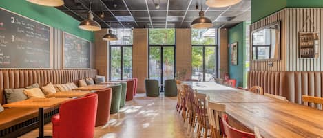 A restaurant with a long wooden counter, red and green cushioned seating, and pendant lighting.