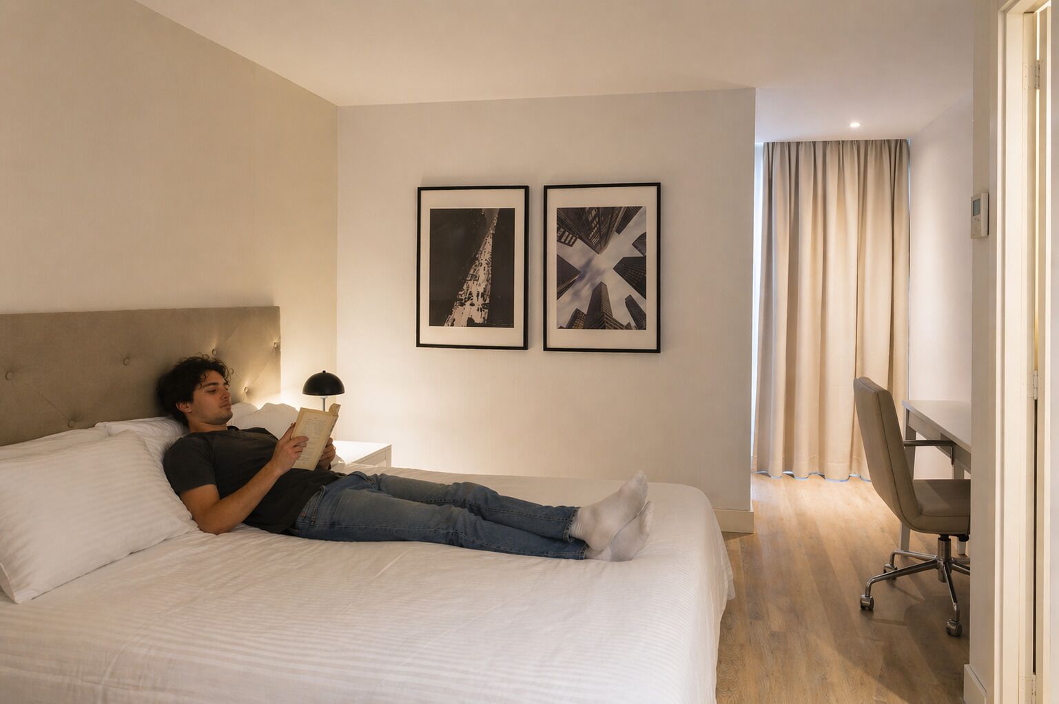 A hotel room with a bed, a desk, and two framed pictures on the wall.