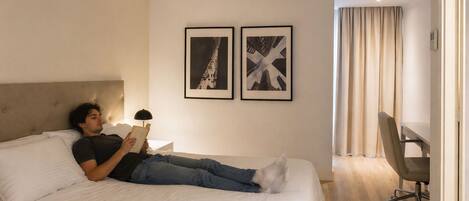 Una habitación de hotel con una cama, un escritorio y dos cuadros en la pared.