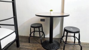 A bunk bed with a small round table and two stools in a room with wooden flooring. - mySTAY BGC North (Makati)