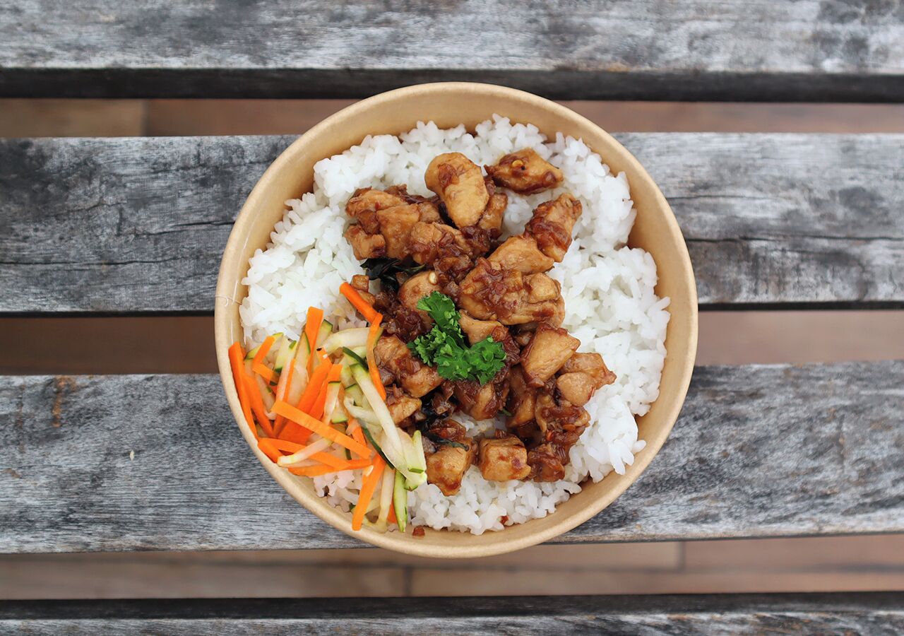 Uma tigela de arroz branco coberta com frango frito e decorada com cenouras e um ramo de salsa.