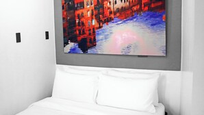 A modern hotel room with a large bed, white bedding, and a vibrant cityscape painting on the wall. - mySTAY BGC North (Makati)