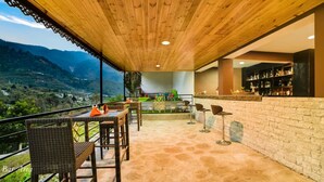 A bar area with wicker chairs and a bar counter, overlooking a mountainous landscape. - Orsino Khangri Karpo Retreat & SPA (Lachung)