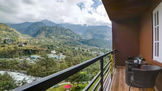 A balcony with a view of a mountainous landscape, including terraced fields and a river. - Orsino Khangri Karpo Retreat & SPA (Lachung)