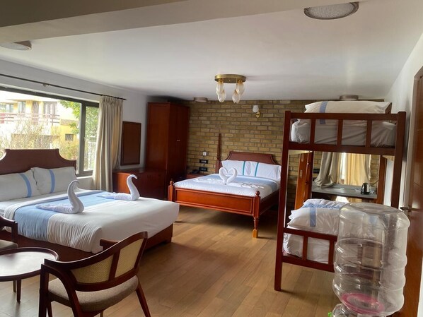 A hotel room with two beds, a bunk bed, a dining table, and a large water dispenser.