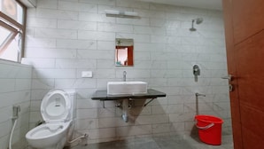 A bathroom with a toilet, sink, mirror, and shower. - RS Family Stay  (Kodaikanal)
