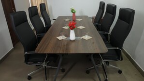 A conference room with a wooden table, black chairs, a white vase with flowers, and a framed picture on the wall. - RS Family Stay  (Kodaikanal)