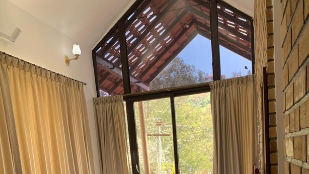 A bedroom with a bed, a seating area, and a view of the outdoors. - RS Family Stay  (Kodaikanal)