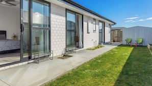 A modern house with large glass doors, a patio with a bed and chairs, and a well-maintained lawn. - Blenheim Accommodation (Blenheim)