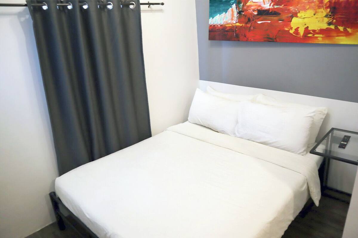 A single bed with white bedding, a gray curtain, and a small bedside table with a remote control.