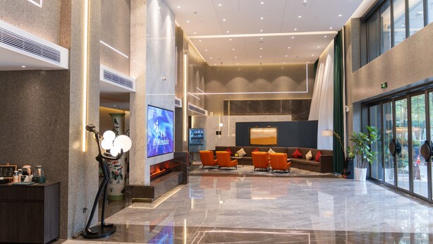 A spacious lobby with a modern design, featuring a seating area with orange chairs, a fireplace, and a large TV screen. - NanNing Mandala Hotel (Nanning)