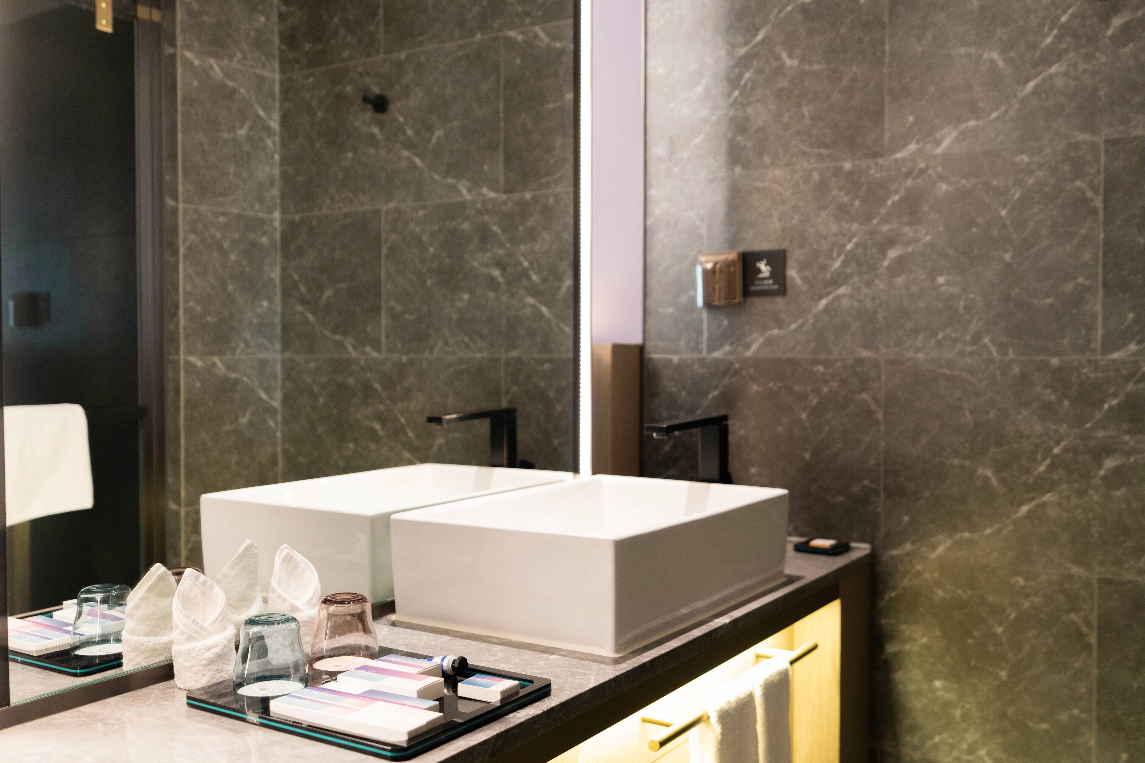 A modern bathroom with two sinks, a large mirror, and a marble wall.