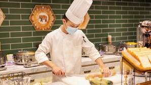 A chef in a white uniform and hat preparing food at a counter with various kitchen utensils and ingredients. - NanNing Mandala Hotel (Nanning)