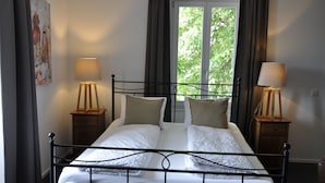 Ein ordentlich bezogenes Bett mit weißen Leinentüchern, zwei Nachttische mit Lampen, ein Fenster mit Vorhängen und ein Gemälde an der Wand.