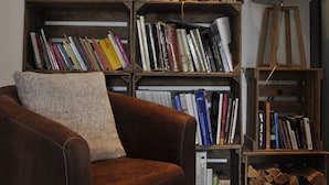 Ein gemütliches Wohnzimmer mit einem braunen Ledersessel, einem Bücherregal voller Bücher und einer Lampe.
