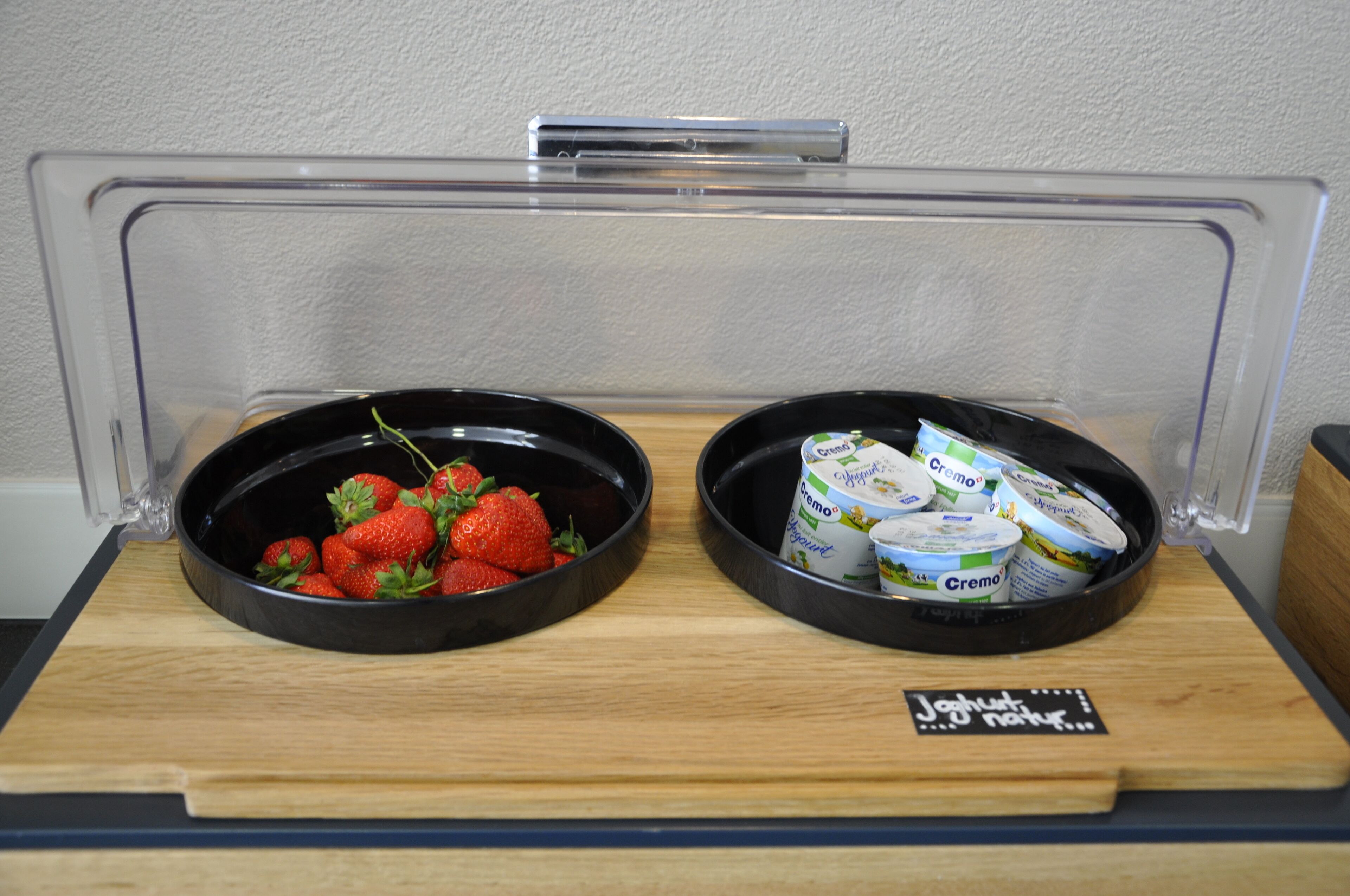 Een ontbijtbuffet met twee schalen, waarvan er een aardbeien bevat en de andere yoghurtbekers.