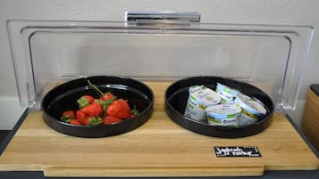 A breakfast buffet with two bowls, one containing strawberries and the other with yogurt cups.